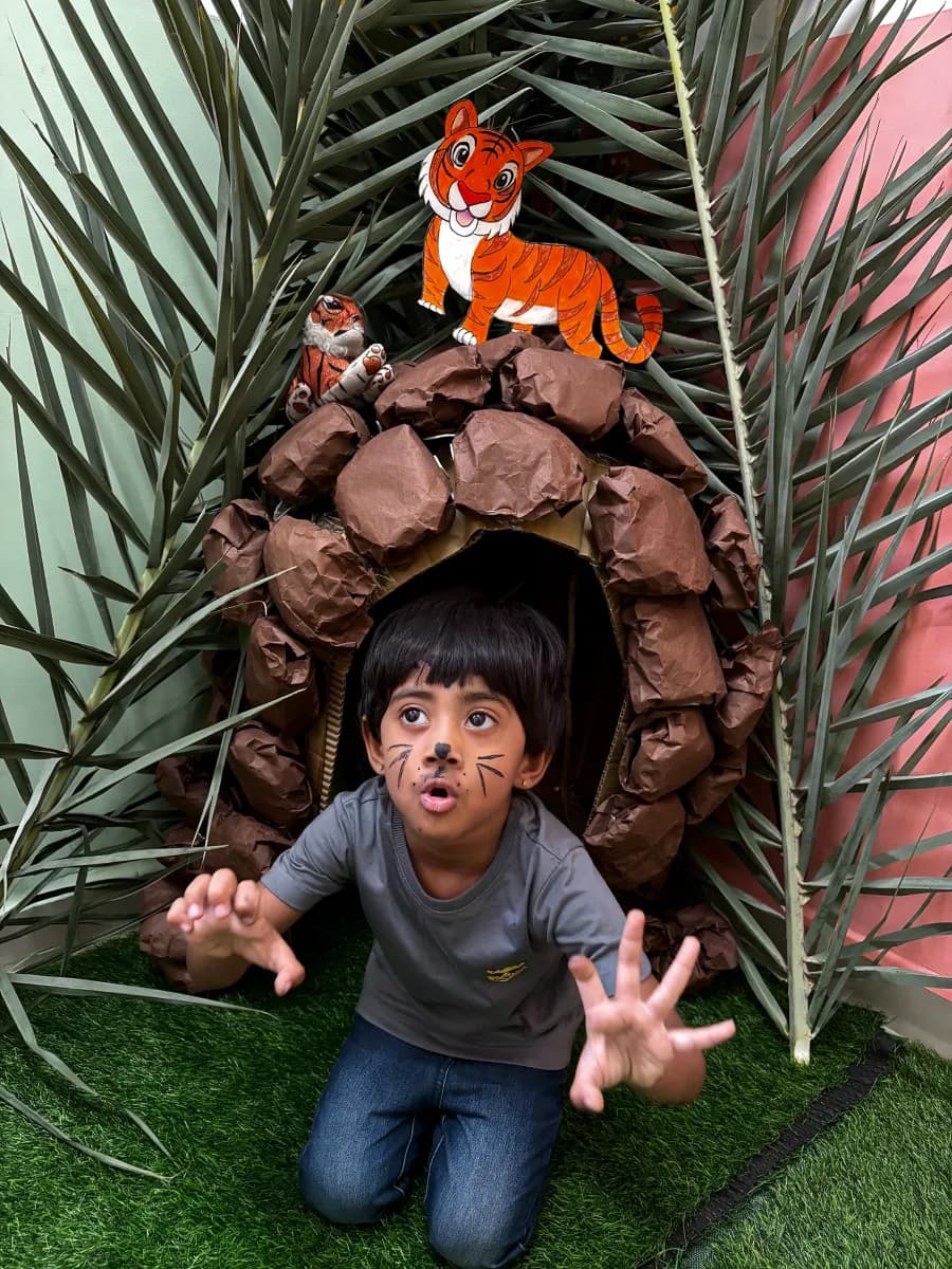 Child with painted tiger whiskers emerging from a jungle cave during Tiger Day celebration